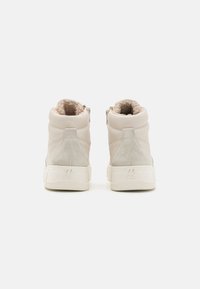Sneakers typu mid-top w jasnym beżowym skórzanym i zamszowym wykończeniu. Teksturowana podszewka kołnierza, solidna biała gumowa podeszwa, subtelne logo na pięcie.