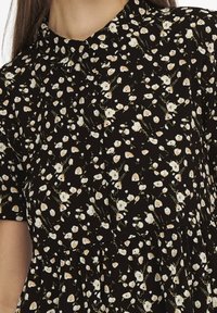 Abito in tessuto nero con motivo floreale bianco e beige. Presenta un colletto, maniche corte e un dettaglio in vita arricciato.