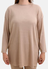 Beige ribbet langærmet top med rund halsudskæring, afslappet pasform og sidelæg. Har et blødt, tekstureret stof og en løs design.