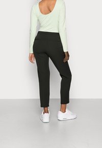 Zwarte op maat gemaakte broek met een slim fit en enkellengte, gecombineerd met een lichtgroene top met lange mouwen en een scoop rug. Witte sneakers.
