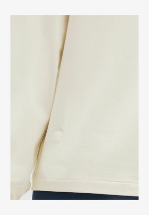 Cream-colored sweatshirt with a textured fabric, a loose fit, and an embroidered logo detail at the hem.