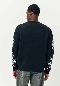 Maglione lavorato a maglia blu navy con motivi a fiocco di neve bianchi sulle maniche. Polsini e orlo a coste, vestibilità regolare, texture morbida.