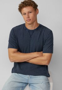 Marineblaues kurzärmeliges T-Shirt aus einem strukturierten Stoff mit rundem Halsausschnitt und verstärkten Schulternähten, kombiniert mit hellen Jeans.