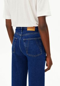 Blaue Jeans aus Denim mit hohem Bund, zwei Gesäßtaschen und einem Lederetikett mit der Aufschrift "ARMEDANGELS" am Bund. Aus Baumwollmaterial.