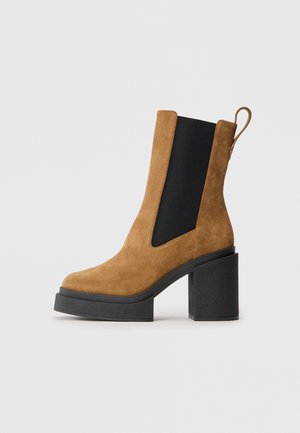 Brown suede ankle boot with a chunky black platform heel and side elastic panels. Features a pull tab for easy wear.