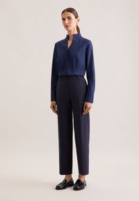 Navy blue long-sleeve blouse with a high collar, paired with tailored navy trousers and black loafers, featuring clean lines and a sleek design.