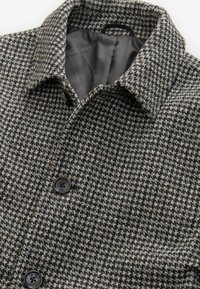 Cămașă din lână cu un model houndstooth în nuanțe de gri și maro, având un guler și două nasturi negri. Captuseala interioară este gri.