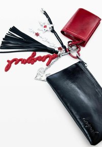 Cartera de cuero negro con cremallera, que incluye cadena plateada, llavero rojo, flecos negros y una mini cartera roja. Los detalles incluyen estrellas y un corazón.