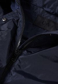 Giacca zippata blu navy con fodera interna, caratterizzata da una texture liscia, etichetta cucita e una cerniera nera lungo un lato.