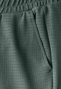 Gevlochten joggers in gedempt groen met een gestructureerd, ruitpatroon. Voorzien van een elastische tailleband en een zijzak voor extra functionaliteit.