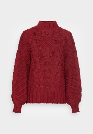 Maglione rosso lavorato a maglia con collo alto, motivi a treccia e dettagli testurizzati. Le maniche a sbuffo e l'orlo a coste aggiungono dimensione.