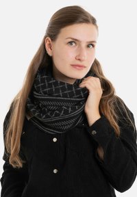 Zwarte infinity sjaal met grijze geometrische patronen, gemaakt van een zachte stof, gedragen om de nek door een model gekleed in een zwart shirt.