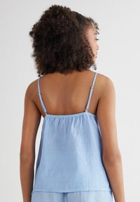 Lichtblauwe, gestreepte cami met dunne verstelbare straps en een losse pasvorm. Gemaakt van zachte stof met een gladde textuur, met geraffineerde details aan de achterkant.
