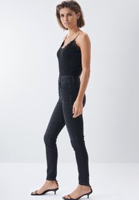 Top básico negro de canalé con encaje, combinado con jeans skinny negros de cintura alta y sandalias de tacón abierto negras.