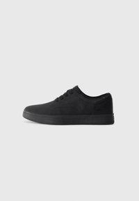Zapatillas negras hechas de un material suave con un diseño de perfil bajo, que presentan cordones planos y una suela de goma texturizada.