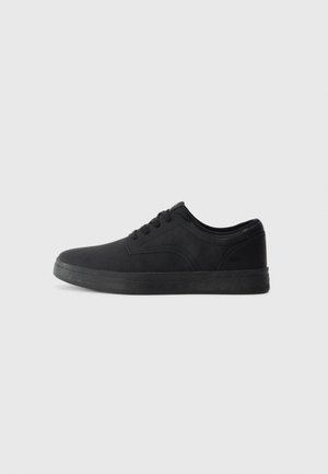 Zapatillas negras hechas de un material suave con un diseño de perfil bajo, que presentan cordones planos y una suela de goma texturizada.