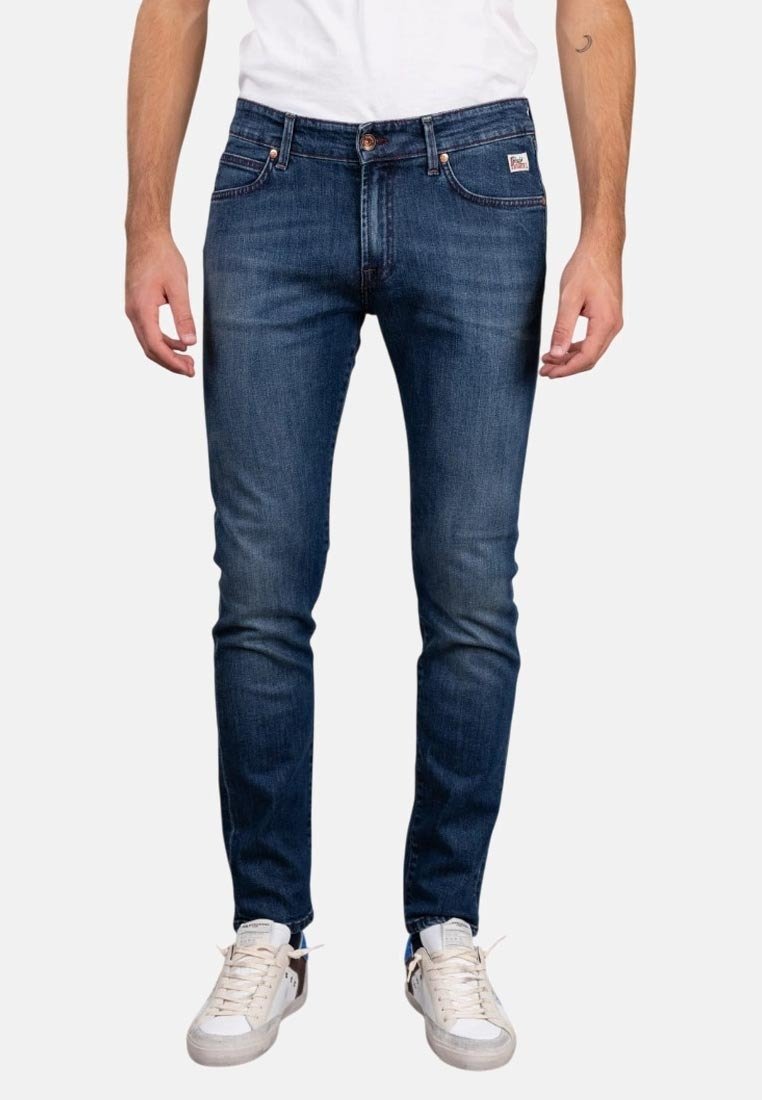 Jeans in denim blu scuro con una vestibilità slim, sfumature sottili, design a cinque tasche e chiusura classica a bottone e zip. Indossati con sneaker bianche.
