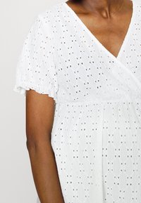 White short-sleeve dress with a V-neck, made of textured fabric featuring eyelet patterns and gathered waist detail.