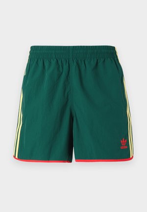 Zelené sportovní šortky s lehkým materiálem, s žlutými bočními pruhy a červenými akcenty na lemu, s malým červeným logem.