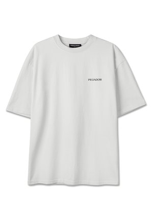 T-shirt blanc uni oversize à manches courtes avec le logo texte "PEGADOR" sur la poitrine gauche et une étiquette à l'intérieur du col.
