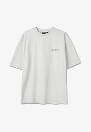 Prosty, biały, oversize T-shirt z krótkimi rękawami oraz logo tekstowym "PEGADOR" na lewej piersi i metką wewnątrz kołnierzyka.