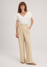 Witte V-hals top met gestructureerde schouderaccenten, gecombineerd met hooggeknipte, wijde beige broeken. Inclusief zakken, gladde stof.