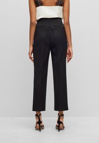 Černé kalhoty na míru s rovnými nohavicemi, vyrobené z hladké látky. Mají dvě zadní kapsy a jemné záhyby.