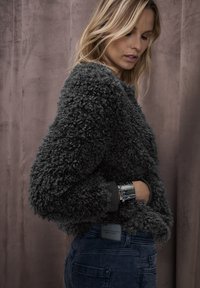 Maglione grigio peloso con finitura testurizzata, scollo rotondo e polsini a coste, abbinato a jeans blu scuro con un'etichetta sul retro.