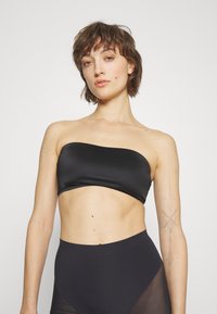 Čierny bandeau top vyrobený z hladkej, elastickej látky. Disponuje jednoduchým dizajnom bez ramienok, vhodný s čiernymi vysokými nohavicami.