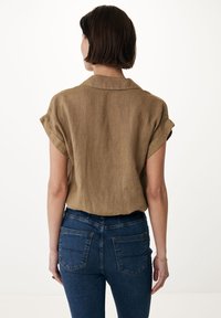 Camicia di lino marrone a maniche corte con colletto, abbinata a jeans in denim blu scuro con tasche posteriori e design aderente.