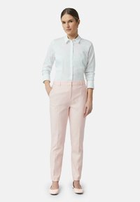 Camicia bianca con bottoni e maniche lunghe abbinata a pantaloni rosa chiaro su misura. Le scarpe sono rosa chiaro con un accento nero. Design semplice.