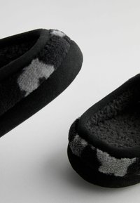 Chaussons noirs avec une doublure en polaire douce et texturée. L'extérieur présente un motif tacheté gris et noir le long du bord.