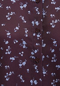 Brown fabric blouse featuring small blue floral print, buttoned front, and short sleeves. Soft texture with a smooth finish.