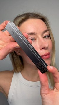 Femme aux cheveux clairs tenant un crayon fard à paupières noir Anastasia Beverly Hills Glidr près de son visage, portant un haut blanc sans manches.