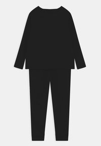 Top negro de manga larga con escote redondeado y ajuste holgado, combinado con pantalones negros ajustados a juego que presentan costuras curvas y puños.