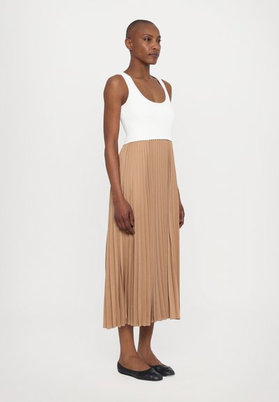 Abito a tank con corpo a costine bianche e gonna plissettata beige. Tessuto morbido, lungo fino alla caviglia, indossato con ballerine nere.