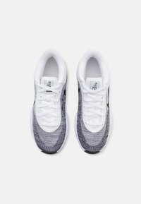 Baskets de sport avec une tige en tricot dans des nuances de gris et blanc, présentant une semelle blanche, un design à lacets et un logo noir subtil sur le côté.