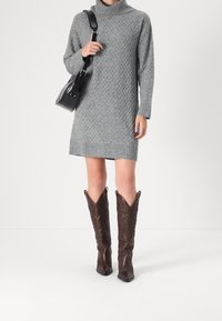 Šedé pletené šaty s rolákem a texturovaným vzorem, doplněné hnědými koženými kovbojskými botami s ozdobným prošíváním.