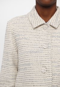 Heled värviga jakk tekstureeritud triibupatterniga koorevalges ja sinises. Omab kraed ja kolme nuppu ees.