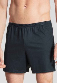 Zwarte zwembroek gemaakt van soepele stof, met een elastische tailleband en een klein label aan de voorkant. Eenvoudig, onversierd ontwerp.