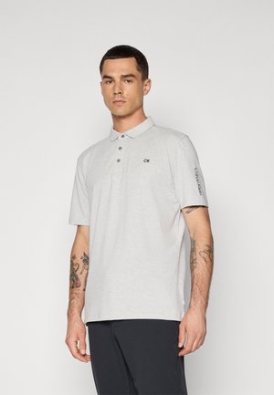 Grå kortermet poloskjorte laget av glatt stoff, med tre knapper og en liten "CK"-logo på brystet, samt tekst på ermet.