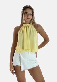Top giallo a halter con un davanti drappeggiato, abbinato a una mini gonne di jeans bianchi con chiusura a bottoni diagonale e orlo sfrangiato.
