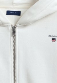 Lichtgrijze zip-up hoodie van een katoenmengsel. Voorzien van een zilveren rits en geborduurd GANT-logo op de borst. Gelaagde afwerking.