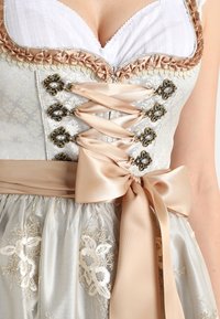 Robe dirndl bleu clair avec un corsage à lacets, un ruban en satin et des détails floraux brodés sur la jupe. Comprend des accents métalliques.