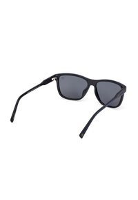 Occhiali da sole neri con lenti grigie, finitura opaca, forma leggermente curvata, con accenti blu sulle tempie, dotati di accessori in metallo.