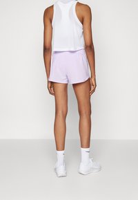 Urheilullinen asu, jossa on valkoinen, hihaton verkkopäällysteinen yläosa ja vaaleanvioletit shortsit. Materiaali näyttää kevyeltä ja sileältä.