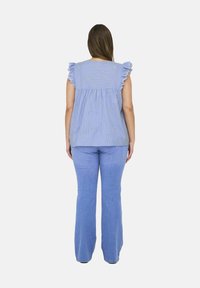 Top a righe blu e bianche con maniche a volant e ricamo floreale sul retro, abbinato a jeans chiari a zampa.