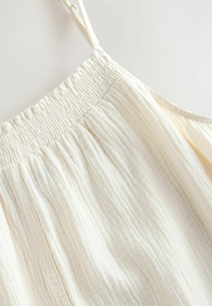 Top senza maniche di un crema chiaro con un bordo elastico arricciato al colletto, caratterizzato da una texture stropicciata e un tessuto morbido e leggero.