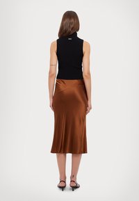 Top negro sin mangas tipo cuello alto combinado con una falda midi de satén marrón, con un diseño envolvente y una textura suave, complementado con tacones negros.