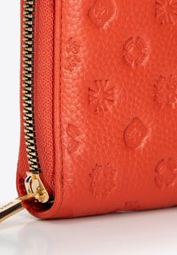 Roodleren portemonnee met reliëfpatronen en een gouden ritsdetail langs de rand. Geprofileerde oppervlakte voegt diepte en visuele interesse toe.